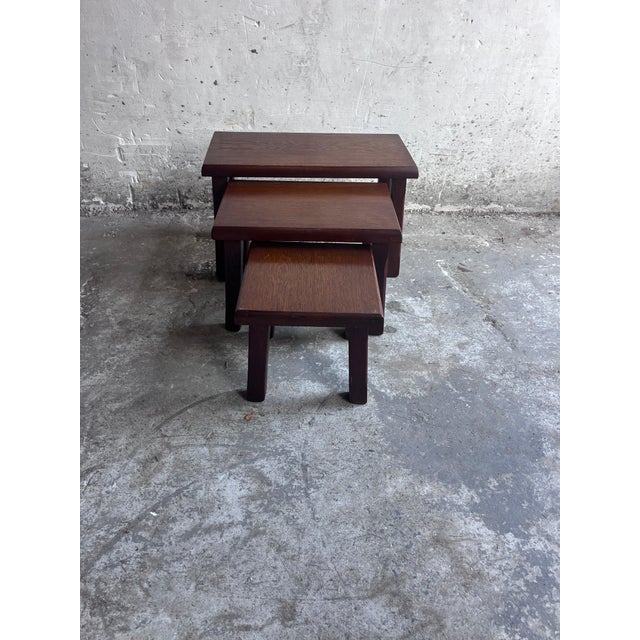A sculptural set of three nesting tables dating from the 1970s. The tables feature warm, dark-stained wooden tops, softly...