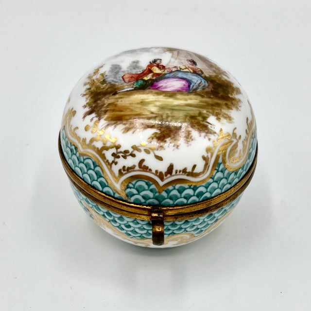 A rare antique porcelain hinged trinket box, hand painted with a romantic Watteau-style scene. This fine round box dates...