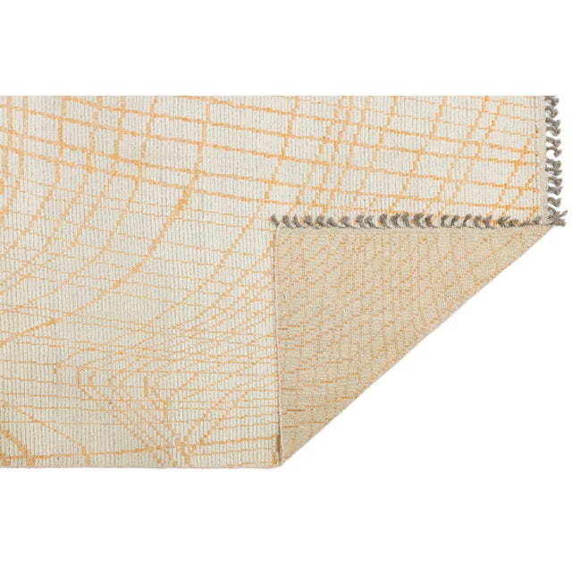 This modern Moroccan-style wool rug features a flowing grid of orange lines over a soft beige field, evoking topographic...