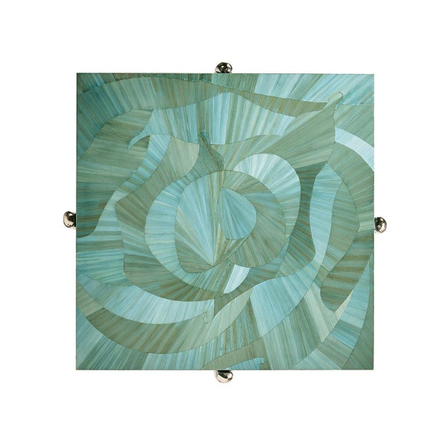 The square top showcases an intricate, hand-applied straw marquetry design, reminiscent of ocean waves in tonal blue hues....