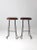 A pair of mid-20th century stools featuring sculptural metal bases with dynamic, curving lines. The fluid silhouette of...