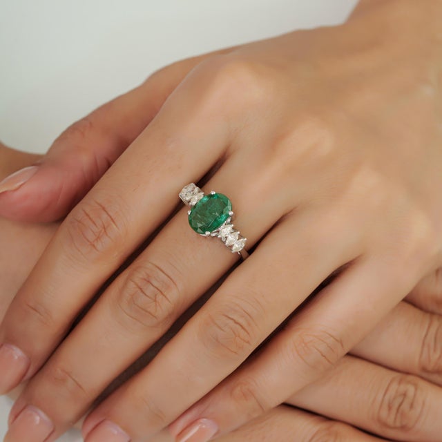 This Modern Mid-Century Style 2.54 Ct Oval Emerald & Marquise Diamond Ring features a striking combination of natural...