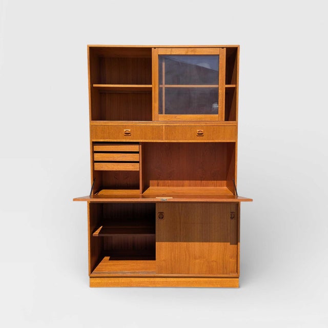 Mid-Century Teak Bookcase with Drop-Front Desk and Lighting. A tall teak wall unit combining open shelving, a drop-front...