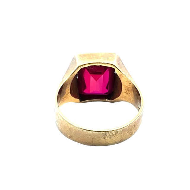 Ring featuring a striking emerald-cut deep red gemstone set in a solid 14K yellow gold mounting. Weighing 6.61 grams and...