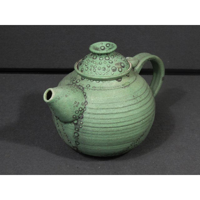 A sculptural handmade studio pottery teapot distinguished by its rounded form, softly ribbed surface, and richly textured...