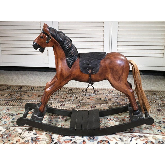 A vintage carved wooden brown painted rocking horse with a black painted mane, natural horsehair tail, tooled leather...