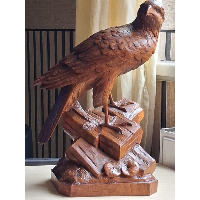 A Black Forest wood carving of an eagle with glass eyes perched on a rocky outcrop, crafted from walnut wood. Masterfully...