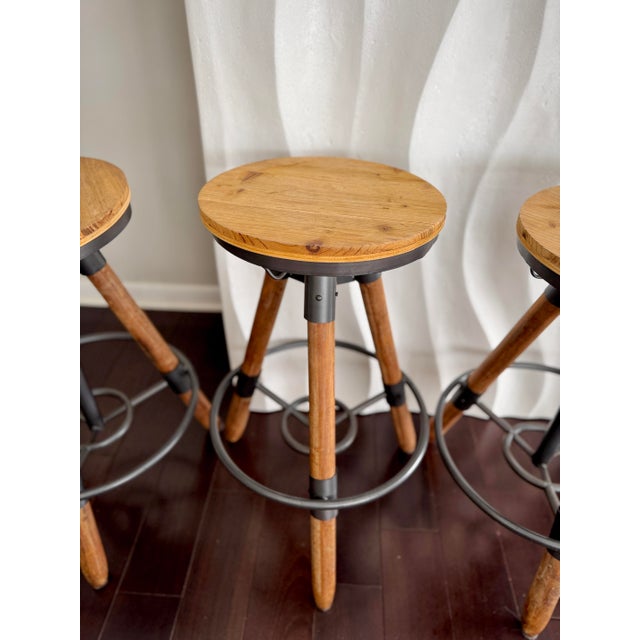 CB2 Set of 4 Industrial Tripod Legs Cb2 Acacia Wood Round Seat Adjustable Counter Stools With Wrought Metal Hardware For Sale - Image 4 of 12
