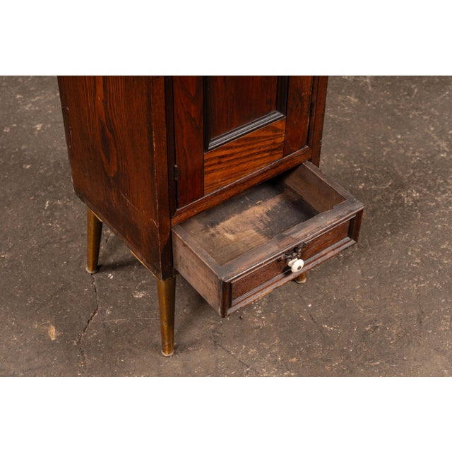 Compact oak cabinet raised on tapered legs with brass caps, combining traditional casework with a slightly elevated, more...