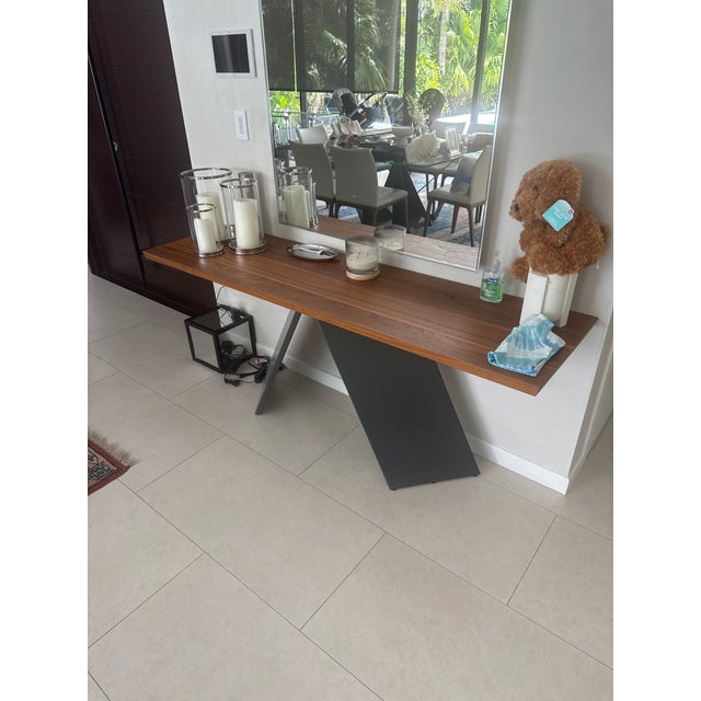 A striking console table featuring a warm medium-toned wood surface paired with a bold, sculptural black base. The...