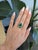A lush Zambian emerald glows at the heart of this pear-shaped ring, its vivid green framed by a delicate trail of...