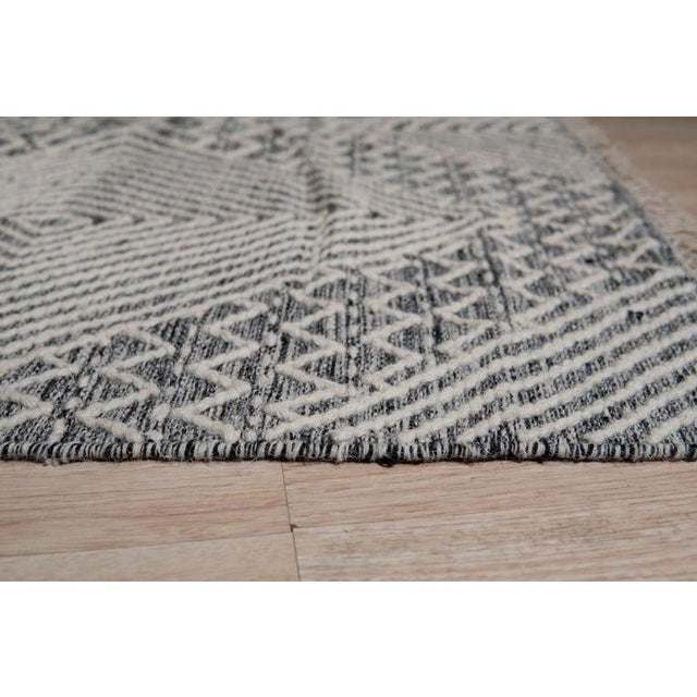 This hand woven wool rug is a black Kilim style floor covering crafted in India. It features a traditional flatweave...