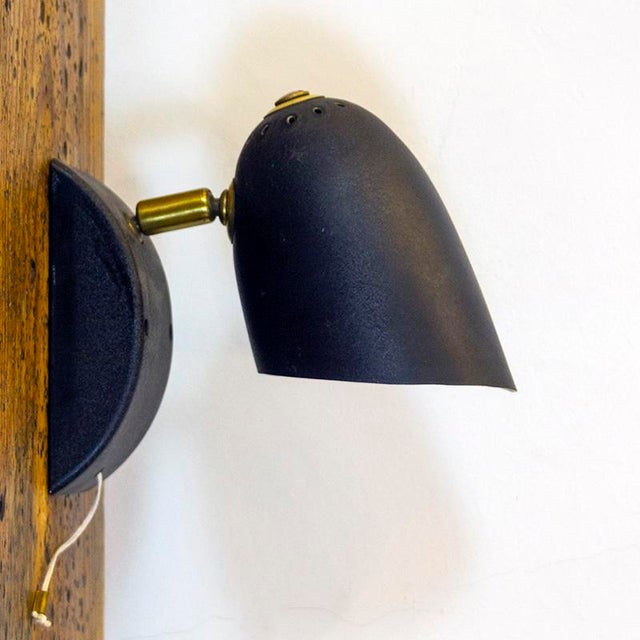 Mid-century Italian black metal wall light with golden brass details. Up to 250V (Europe/UK Standard).The wiring of this...