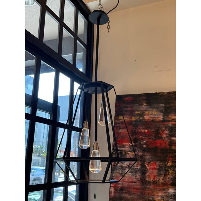 Design Plus Gallery presents a Faceted Geometric Lantern Shape Pendant. An open black metal frame forms an angular,...