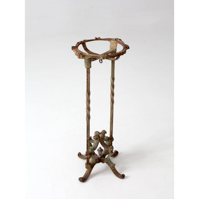 Antique cast iron plant stand with a tall, narrow profile featuring twisted uprights, an ornate scrolled base, and a...