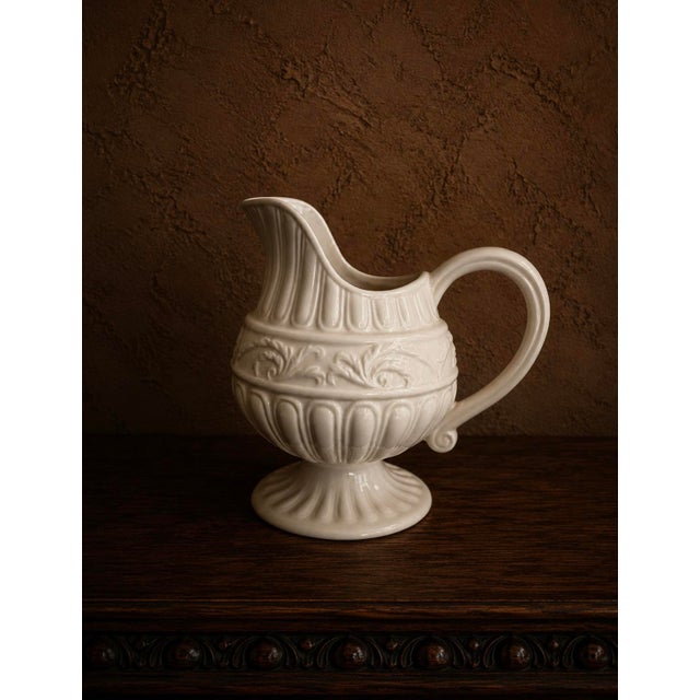 A charming vintage creamware pitcher standing 8" tall. This footed jug features layered embossed relief decoration...