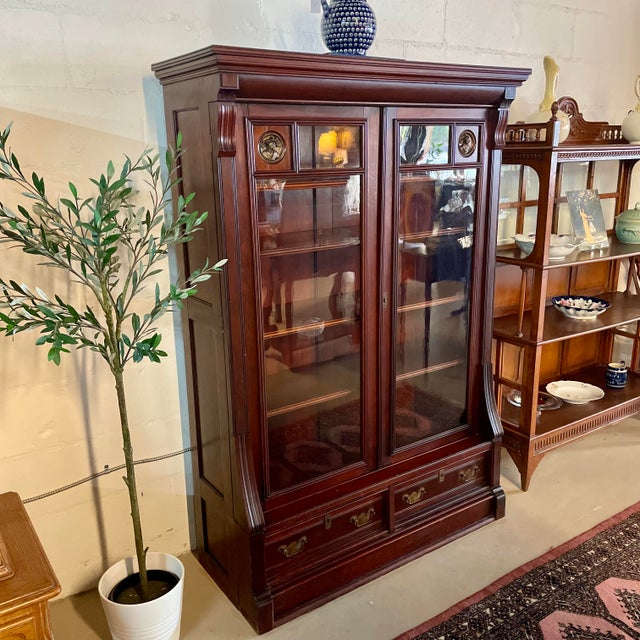 Antique mahogany bookcase with framed glass doors, four interior adjustable shelves, and two drawers below for additional...