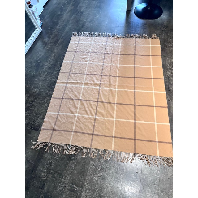 This is a camel-colored windowpane throw blanket featuring a classic large-scale plaid pattern and fringed edges, similar...