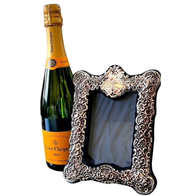 An ornate silverplated tabletop picture frame featuring elaborate scrolling foliage, small blossoms, lattice details, and...