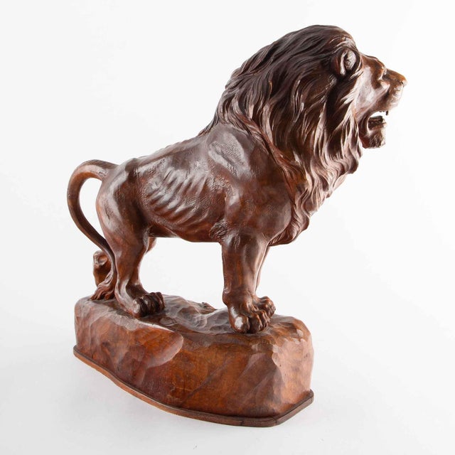 Finely carved wooden sculpture depicting a standing lion poised atop a naturalistic rocky outcrop. Executed with...