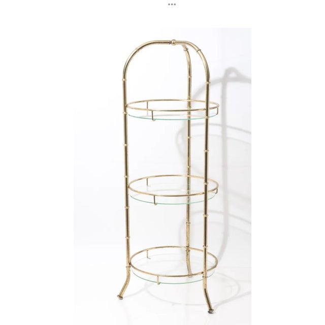 This vintage Hollywood Regency faux bamboo three-tier étagère features a polished brass frame and three circular glass...