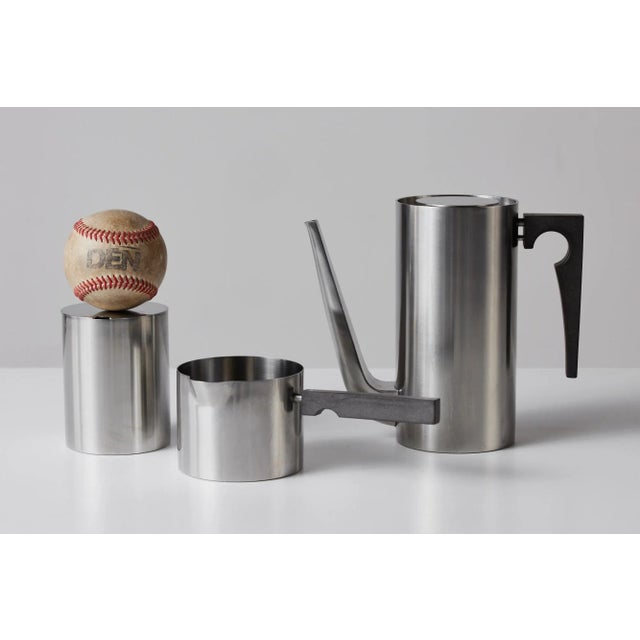 Three piece stainless steel tea set by Arne Jacobsen for Stelton, c.1960s, Denmark. The set includes a tea pot, creamer...
