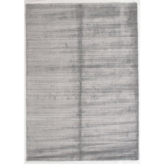 Hand-knotted modern rug featuring a minimalist, textural design with subtle horizontal striations across a soft gray...