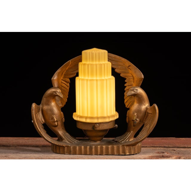 Striking Art Deco table lamp featuring a cast metal base formed by a pair of stylized eagles with wings raised in...