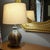 An artisanal mid-century drip glaze mannered ceramic lamp is displayed in tones of olive green, mustard yellow, and...