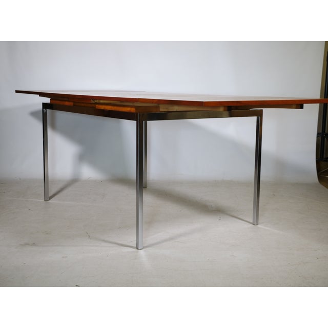 Extendable dining table in walnut with a chrome-plated metal frame from the 1960s. The warm wood surface provides a...
