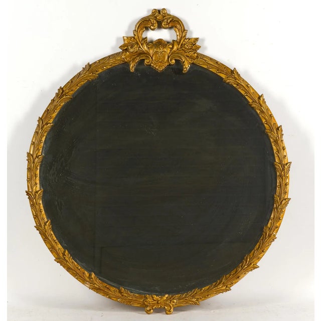 Elegant vintage round giltwood mirror in the Louis XV/Rococo style, featuring beveled mirror glass, a carved foliate...