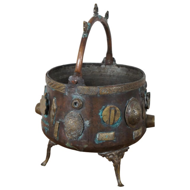 Antique bronze cauldron with tripod base and swivel handle, decorated with etched ornate medallions going along the body....