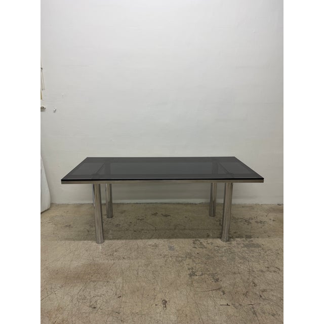 Smoked glass top dining table top on a rectangular chrome base with tubular chrome legs originally designed by Tobia...