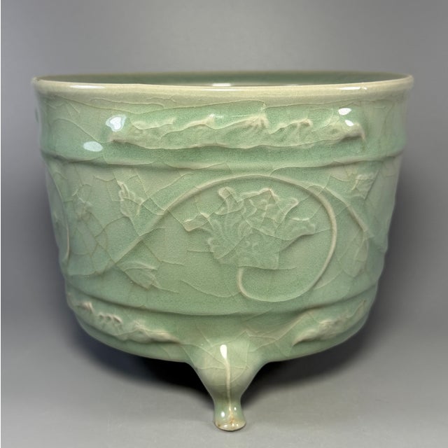 Fine antique Chinese celadon tripod censer. Cylindrical body decorated with carved scrolling floral patterns, supported by...