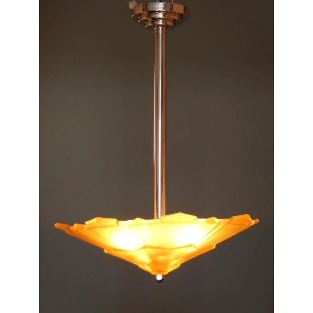 This Art Deco chandelier features a chrome-plated metal bracket with a tiered canopy and an amber-colored glass bowl with...