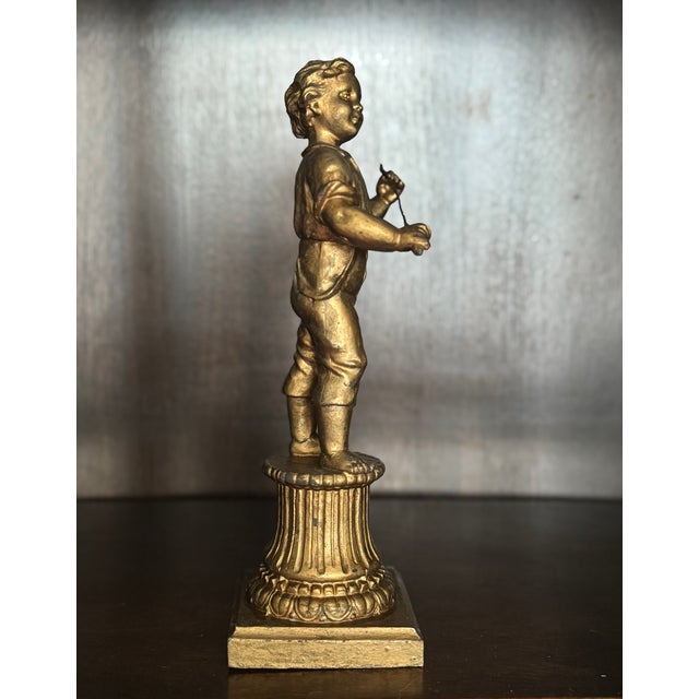 An antique decorative figure depicting a young boy standing atop a fluted classical pedestal. Cast in spelter and finished...