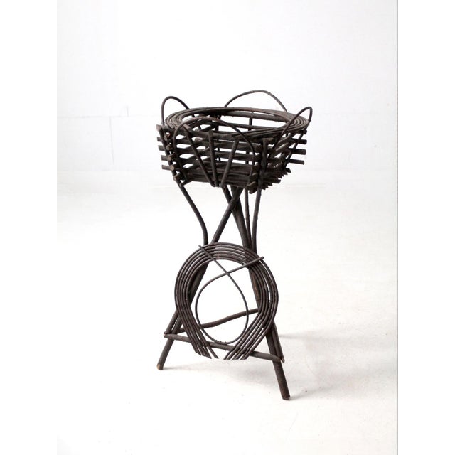 This antique Adirondack twig table plant stand is a rustic American design with a black twig tripod frame, basket-style...
