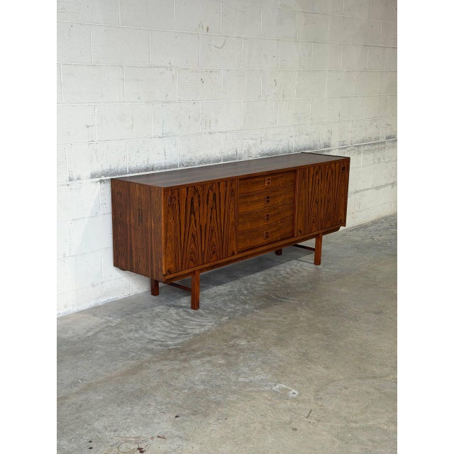 This architectural low sideboard features a minimal profile elevated by a sculpted four-legged trestle base. The...