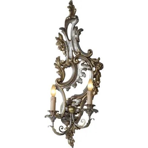Hand carved wood sconce featuring two lights and an acanthus leaf motif in a distressed silver gilt and mecca finish. Italy