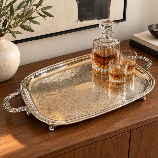 Elegant silver-plated footed serving tray featuring intricate floral and scroll decoration, a smooth central oval for a...