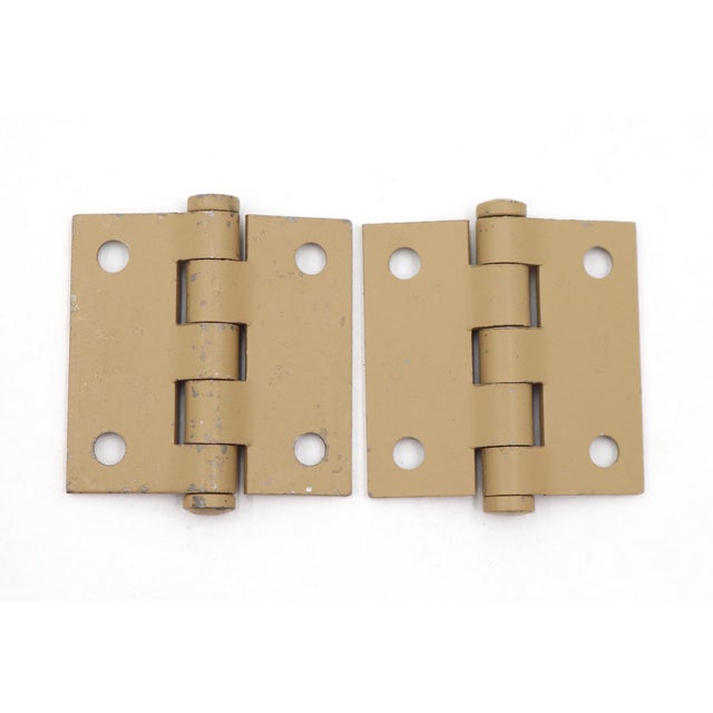 Vintage cabinet door hinges made of painted tan steel. They feature flat tips, five knuckles, and a template hole pattern....