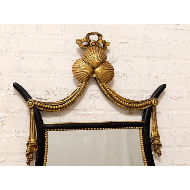 A dramatic vintage wall mirror with an elegant Hollywood Regency feel, featuring a black frame richly accented with gilt...