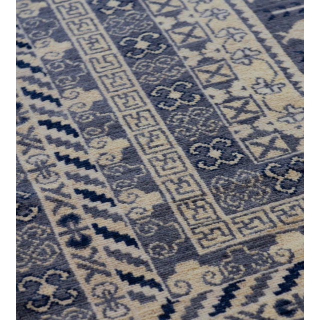 his handwoven Khotan style rug features a shaded charcoal-grey field with an overall design of ivory angular pomegranate...
