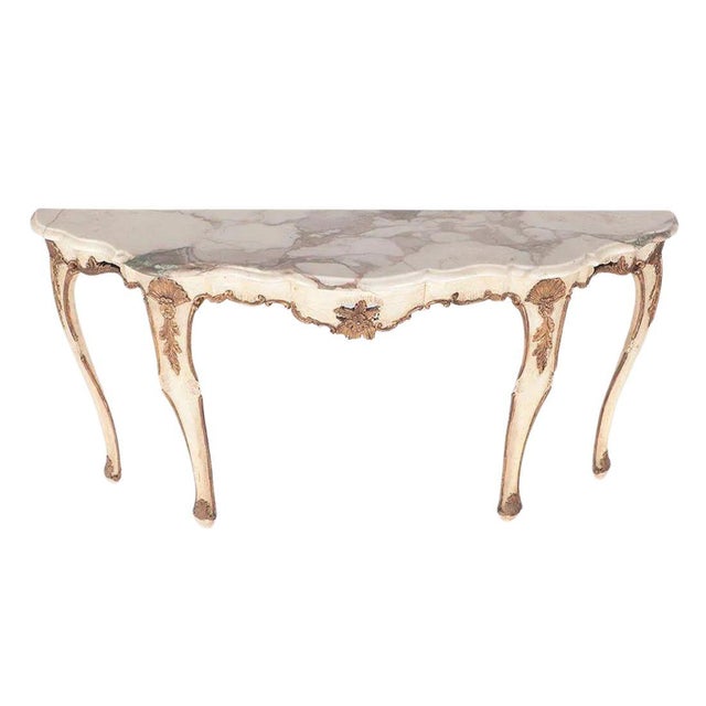 A vintage 1950's parcel gilt and painted marble top demi-lune console table in Regency style. Cream in color with graceful...