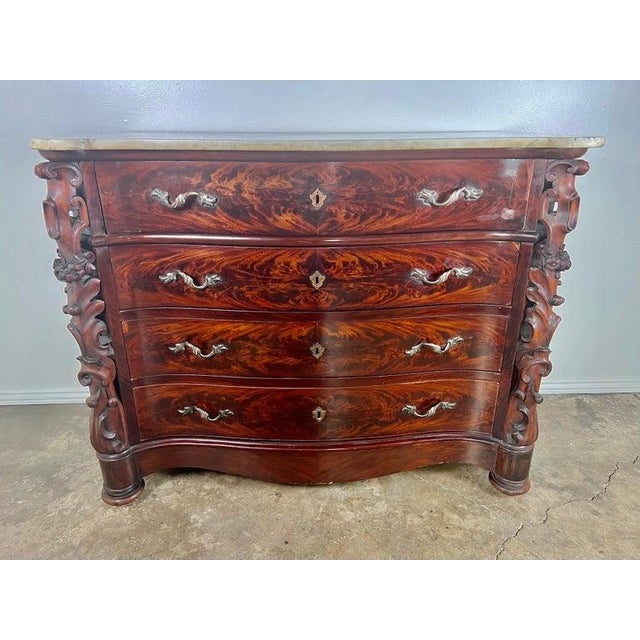 19th century English feathered mahogany chest of drawers. There are finely carved panels flanking the chest that depict...