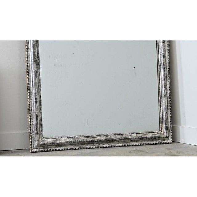 A French, 19th century Louis Philippe mirror in a thick, antiqued silver frame texturized by dark burnishing and...