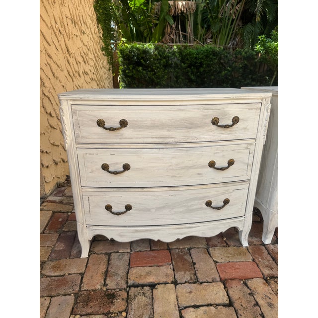Pair of distressed white French chests or bedside tables. Distressed white finish, 3 drawers, metal/ brass hardware.
