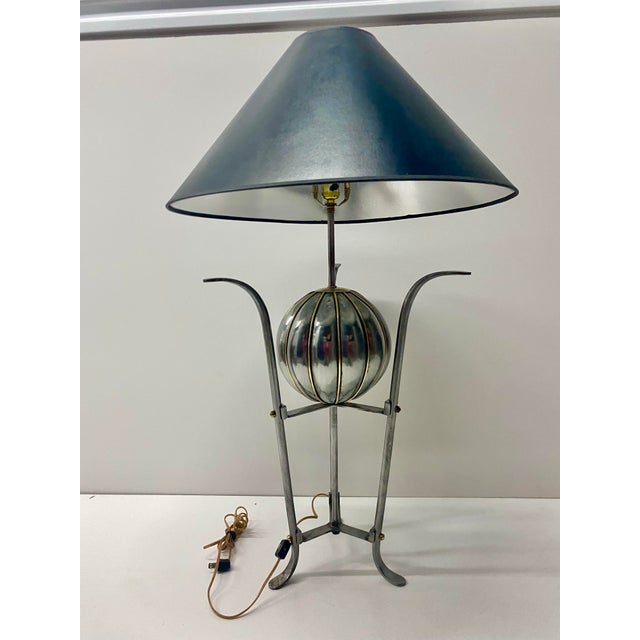 A large, metallic ribbed sphere with a polished finish acts as the visual centerpiece.The lamp is supported by slender...