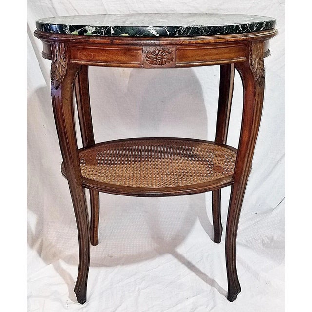 elegant oval French walnut side table with newer marble top, caned shelf on base, acanthus leaf on square channeled...