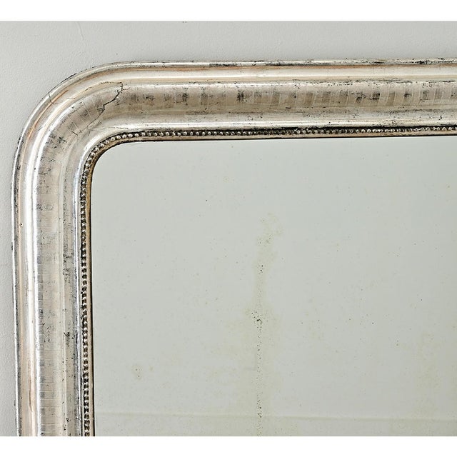 A French 19th century Louis Philippe mantel mirror with an understated, silver gilt frame enhanced by dark oxidation and...
